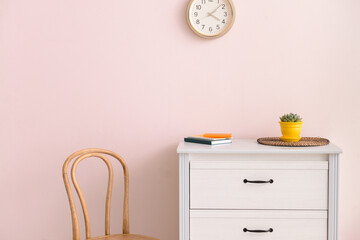 Modern chest of drawers with chair near color wall in room