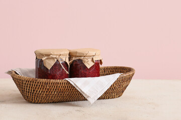 Wicker basket with jars of jam on color background