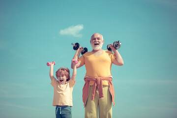 Funny old senior man and kid boy with dumbbells. Sports education. Cute kid and senior man exercising with dumbbells.