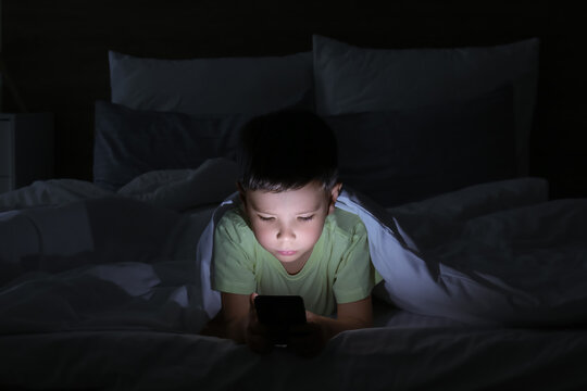 Little boy suffering from sleep disorder with mobile phone in bedroom