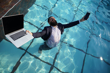 Crazy comic business. Excited business man in suit with laptop and mobile phone on swimming pool....