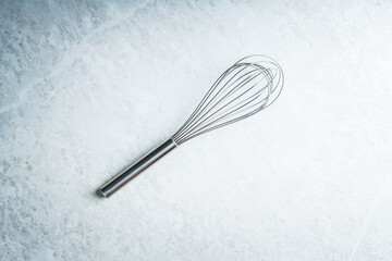 Clean and shiny metal whisk on the white table. Shot form above. 