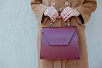 Fashionable young woman wearing beige wool coat and blue jeans. She is holding beautiful leather burgundy handbag. Street style.