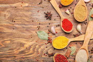 Spoons with different aromatic spices on wooden background