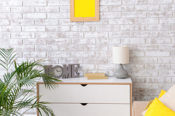 Modern chest of drawers with lamp near brick wall in room