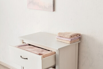 Modern chest of drawers with clean towels near white wall in bathroom