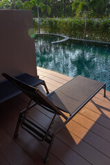 Steel deckchair on wooden poolside terrace with trees background