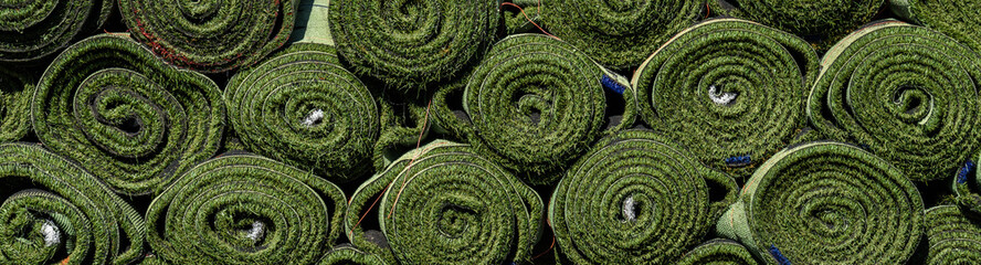 Green rolls of new artificial turf ready for installation on an outdoor sports field
