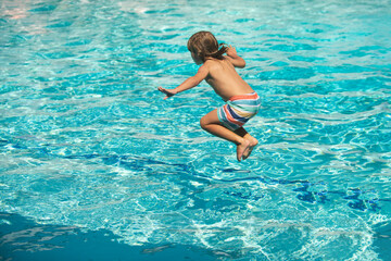 Child jumping in swimming pool. Kid having fun on summer vacation.