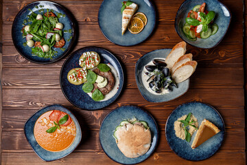 Designer plates on the table, assorted european meals on wooden background, directly above view