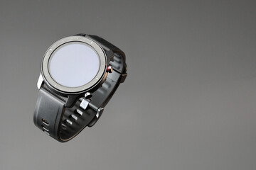 Wireless smart watch in a round matte black case with risks on the rim and a silicone strap on a gray background with space for text.