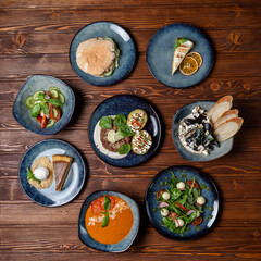Circle of plates on the table, buffet in a restaurant, assorted european meals on wooden background