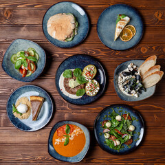 Circle of plates on the table, buffet in a restaurant, assorted european meals on wooden background