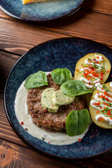 Close up of appetizing and juicy pork patty, grilled with jacket potato and creamy sauce, wooden table of a modern restaurant