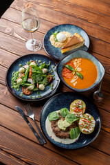 Above view of european lunch on wooden table: gazpacho, meat patty, salad and dessert