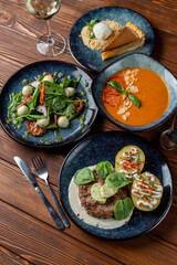 Above view of european lunch on wooden table: gazpacho, meat patty, salad and dessert
