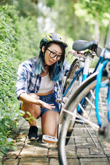 Obraz premium Unhappy young Chinese woman in helmet looking at her broken bicycle