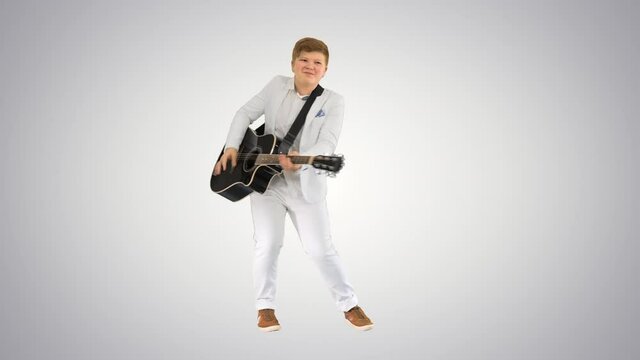 Boy in white playing acoustic guitar and dancing on gradient background.