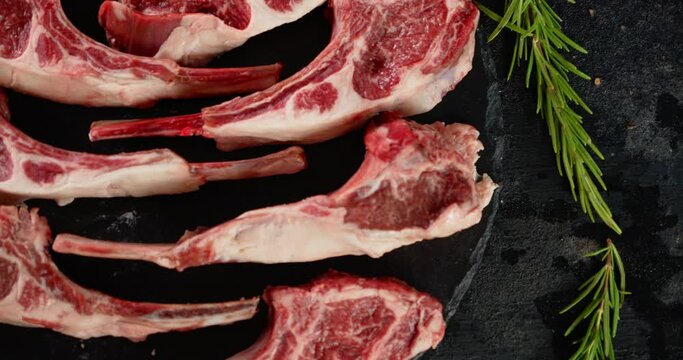 Pieces of raw rack of lamb with rosemary on a stone board.
