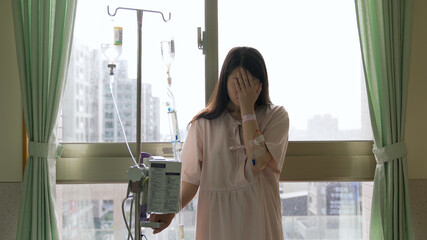 portrait of hospitalized female cancer patient back on window holding iv drip stand and weeping in despair.