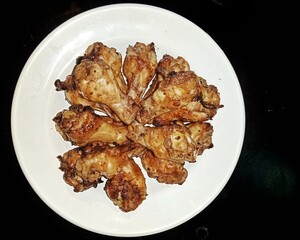 Baked chicken wings in a plate on a black background