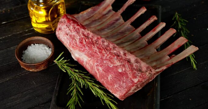 A piece of raw rack of lamb with spices and rosemary. 