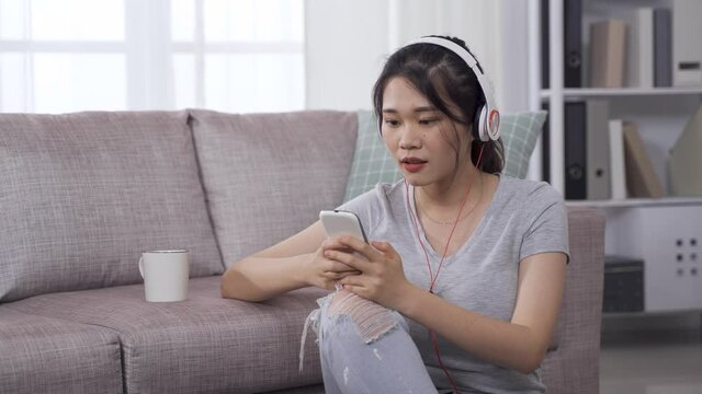 charming asian young woman enjoying online streaming music on mobile phone with head moving and hand swinging.