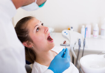Dentist in white is taking a view of an adult woman on the chair in hospital.