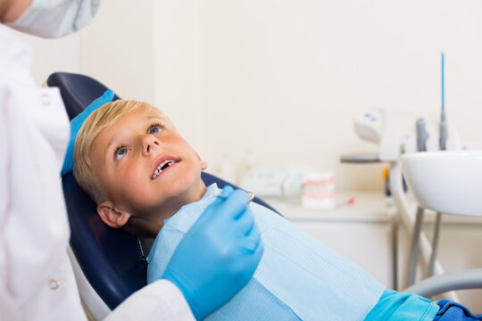 Stomatologist in uniform is taking visional inspection of a child on the chair in hospital.