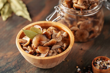Homemade pickled honey agarics in wooden bowl and  open glass jar, spices, spoon, napkin,  on  wooden table. Marinated mushrooms are valuable source of protein. Fermented healthy food.