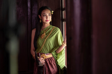 Portrait  of a beautiful woman in Thai old suit or Thai national dress suit looks elegant and charming in Old antique Thai houses/Old Thai fashion model concept