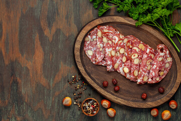 Smoked sausage salami with hazelnuts in a wooden plate on the table. Top view