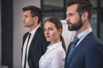 Brown-haired female looking into camera, standing between two male colleagues