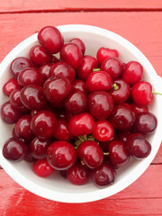 Ripe cherries in a white plate on a red table