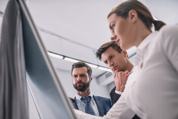 Bottom view of brown-haired female writing on flipchart, male colleagues checking notes