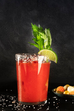 Bloody Mary cocktail with tomato juice, lime, and celery, wiuth pickles, side view on a black background with copy space