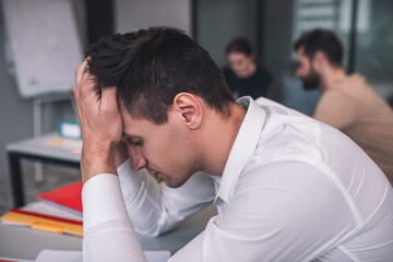 Tired dark-haired male sitting at meeting, resting his head on his hands