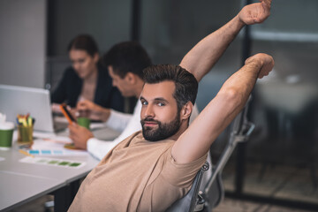 Bearded young male sitting at meeting and stretching