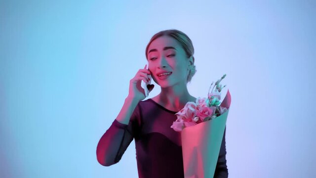Young ballerina with flowers talking on smartphone on blue and pink background