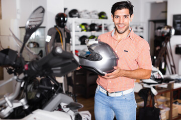 Fototapeta na wymiar Portrait of glad cheerful smiling male customer who is posing in new helmet in the sport store.