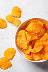 Spicy potato chips in white bowl, gray background, top view. Fast food concept.