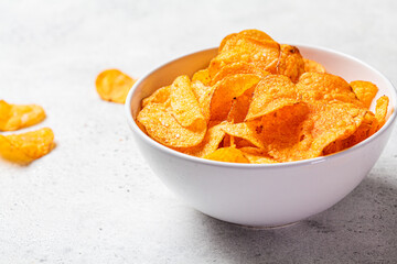 Spicy potato chips in white bowl, gray background. Fast food concept.