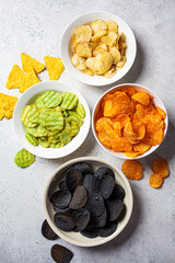 Different types of colored potato chips in white bowls, gray background. Fast food concept.