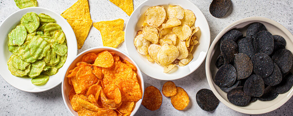 Banner of different types of colored potato chips in white bowls, gray background. Fast food...