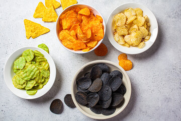Different types of colored potato chips in white bowls, gray background. Fast food concept.