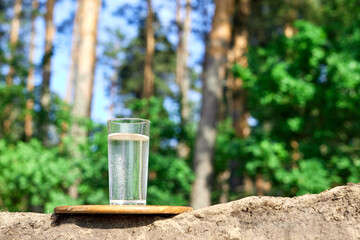 Naklejka premium Glass of cold water on wooden board. Sand and trees with nature background. Clean water concept.