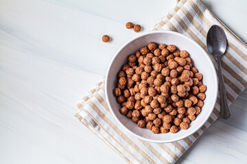 Chocolate balls corn flakes in white bowl, white background. Breakfast food concept.