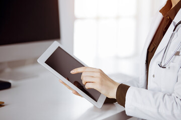 Unknown female doctor using tablet computer in sunny clinic. Perfect medical service in hospital