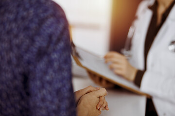Doctor and patient discussing current health examination while sitting in sunny clinic. Perfect...