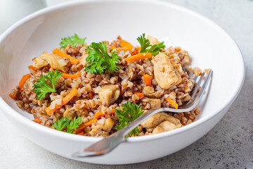 Buckwheat with chicken meat and vegetables in a white plate, white background. Traditional Russian cuisine concept.